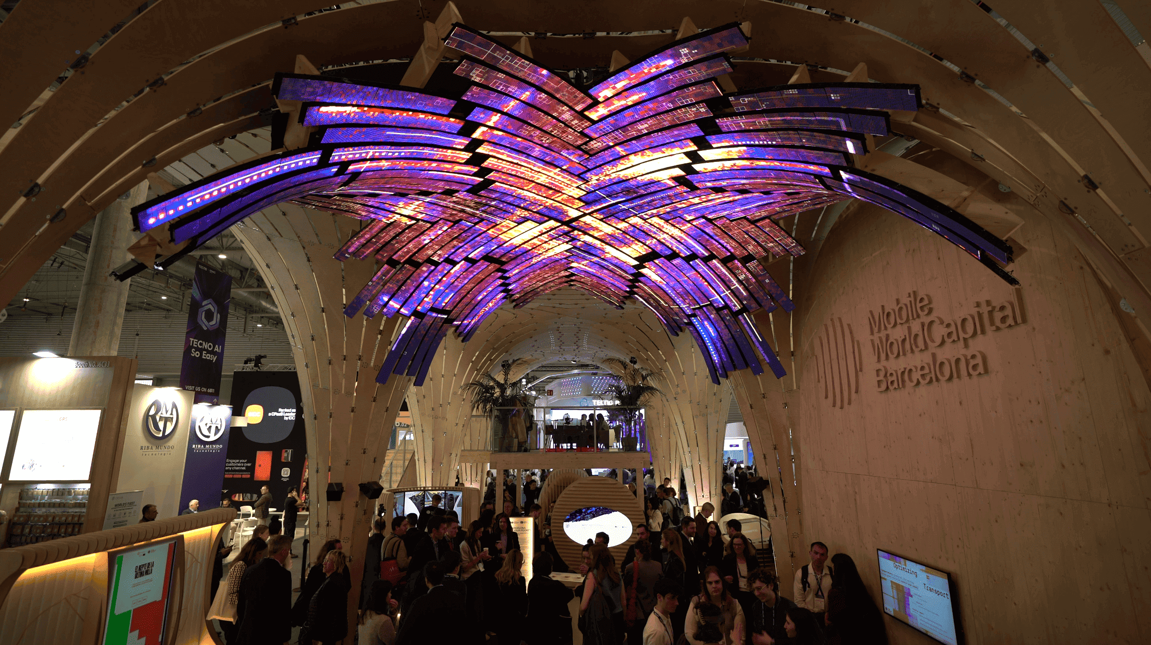 Domo LED del stand de Barcelona World Capital en el MWC 2025, con formas moradas y naranjas sobre la estructura de madera y visitantes debajo.